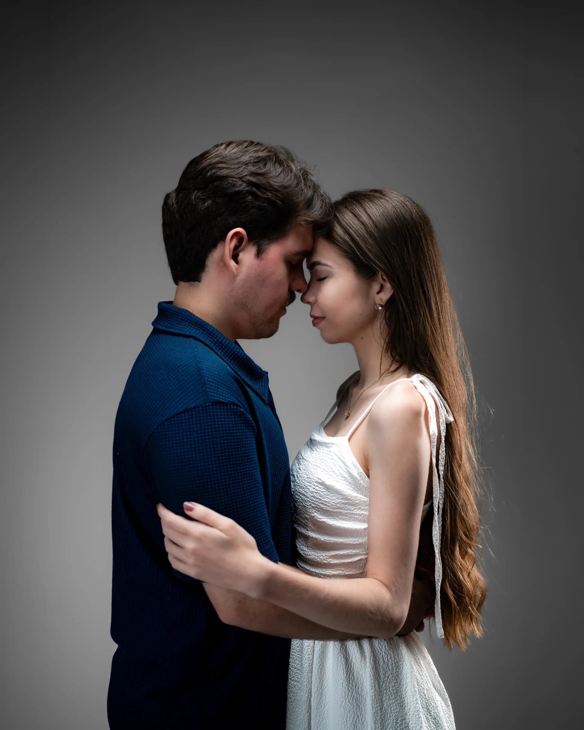 Casal de perfil com as testas encostadas e os olhos fechados, sob luz lateral